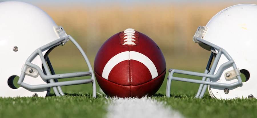 American football placed between two football helmets on field