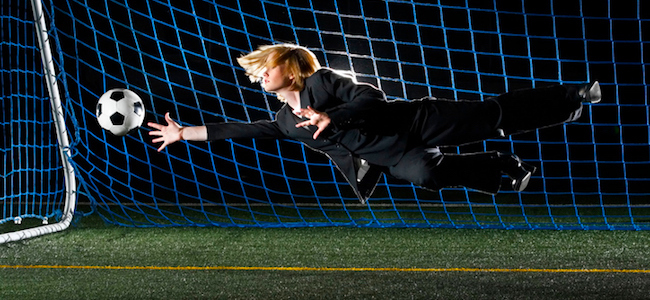 Female football player diving for ball in suit