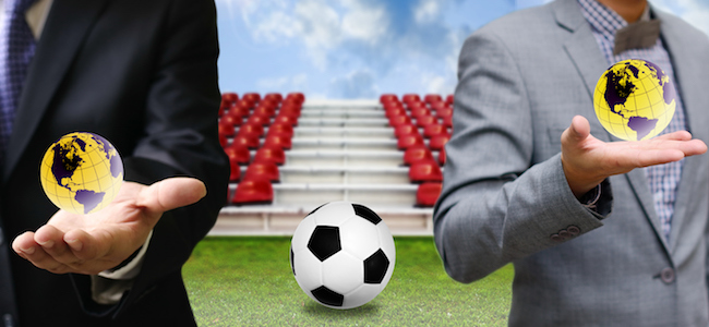 Global football with businessman holding small globes with football in between