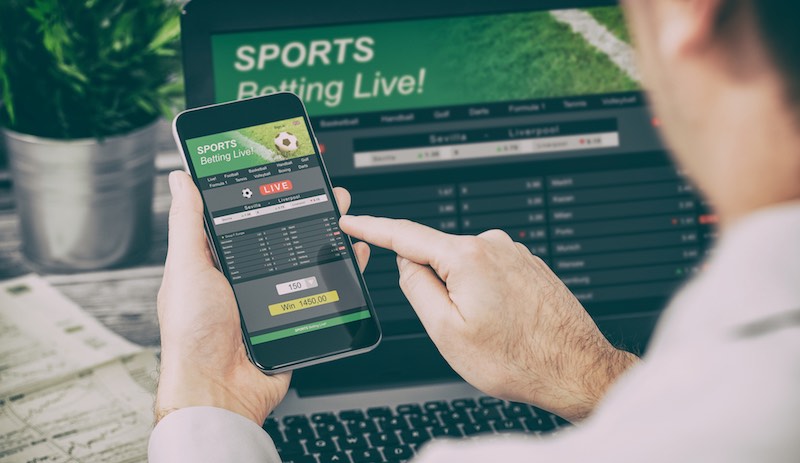 Man betting on sport on a phone with laptop open