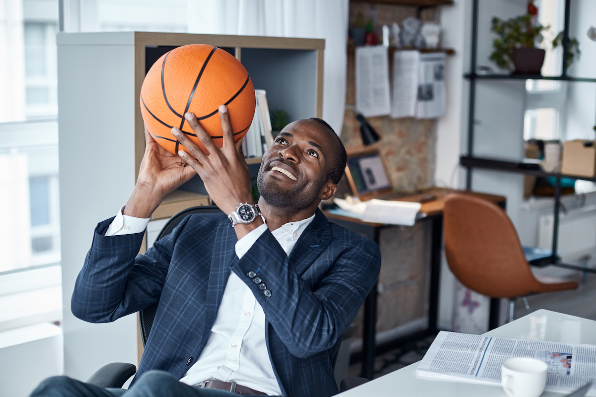 Businessman throwing basketball in the air at his desk. 