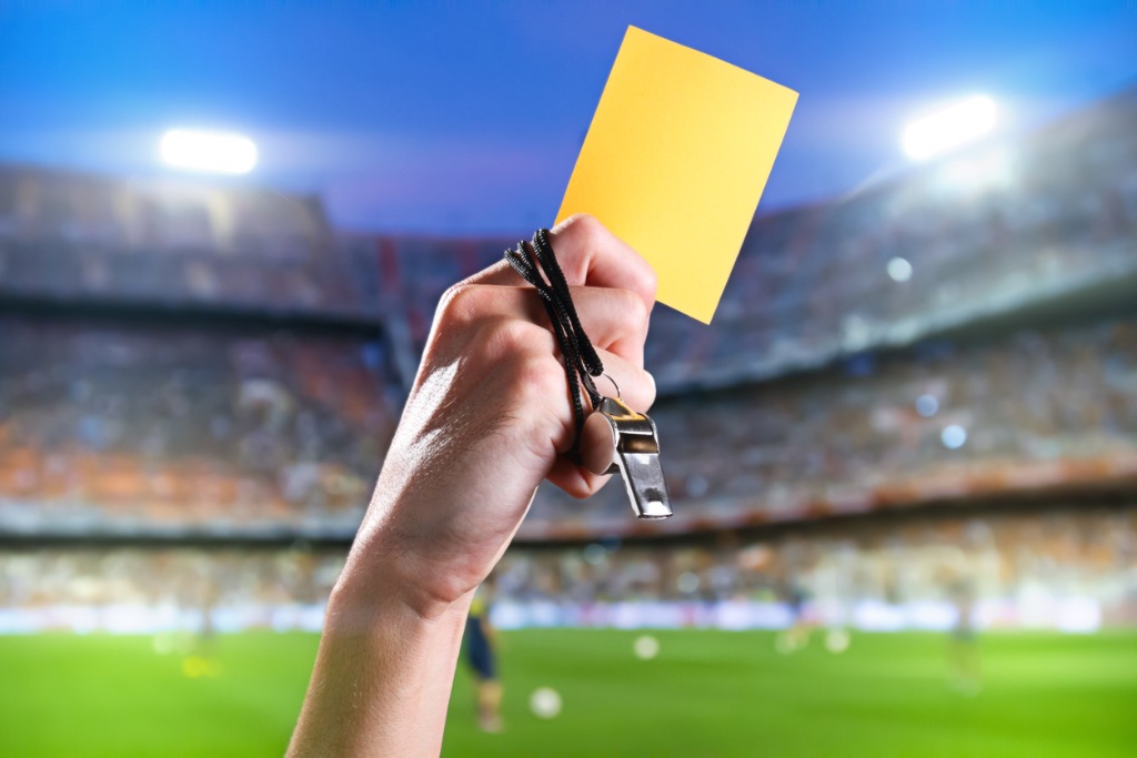 Hand of A Referee With Yellow Card and Whistle